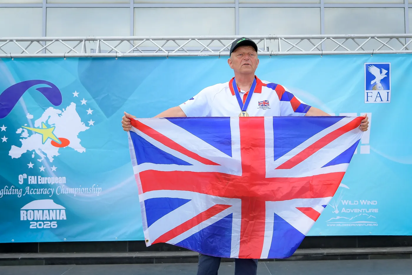 Andy Shaw wearing his bronze medal and holding a Union flag in front of the FAI championship banner