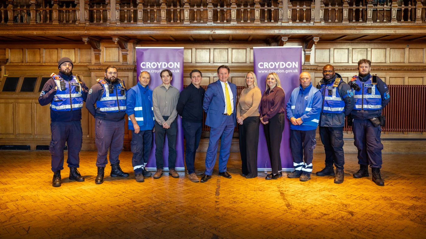 A group in uniform and office clothes stands between two Croydon Council banners in a wood-panelled hall