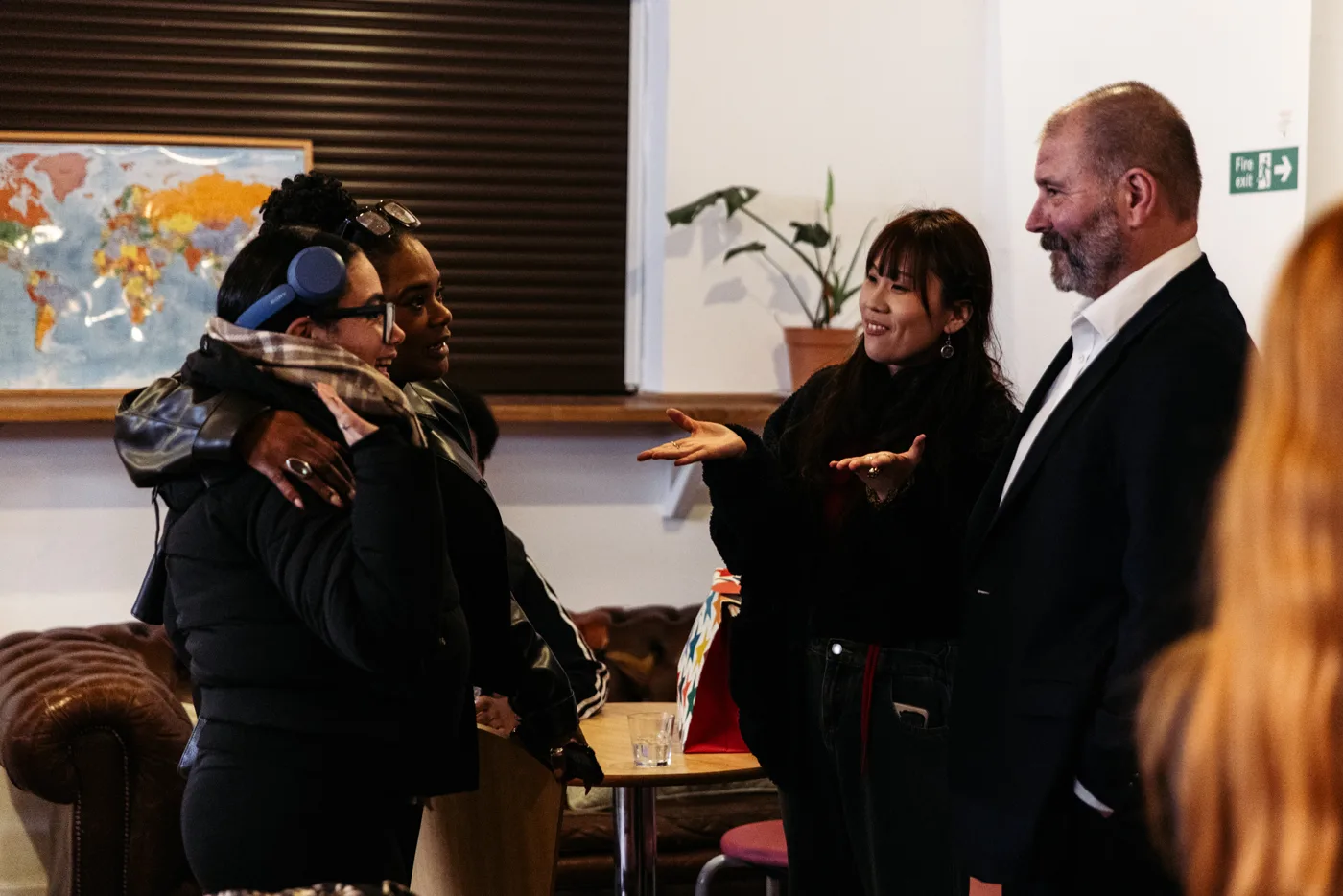 Two young women embracing as they talk with a woman and a man in a suit at the launch