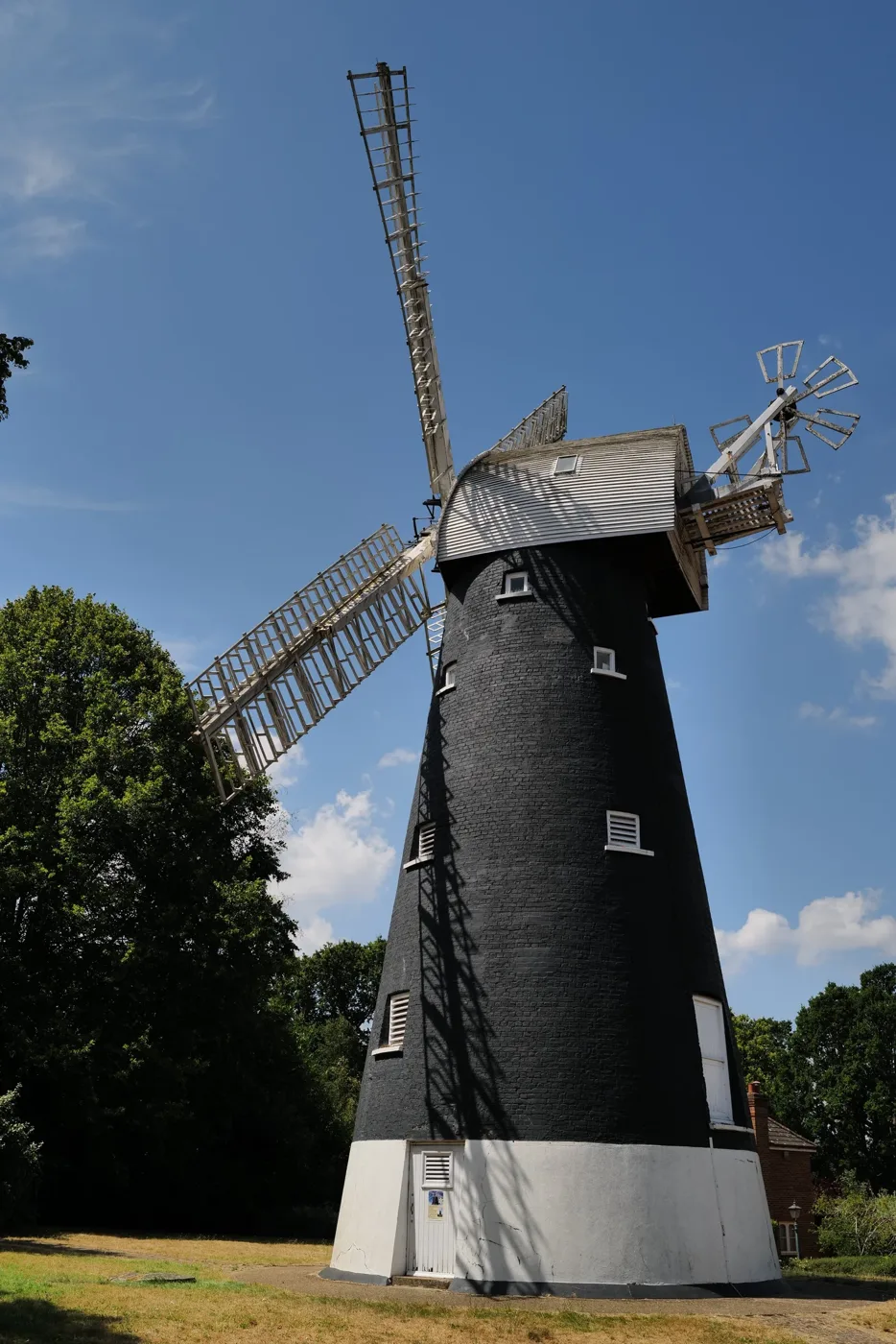 A black-painted windmill with white sails against a blue sky