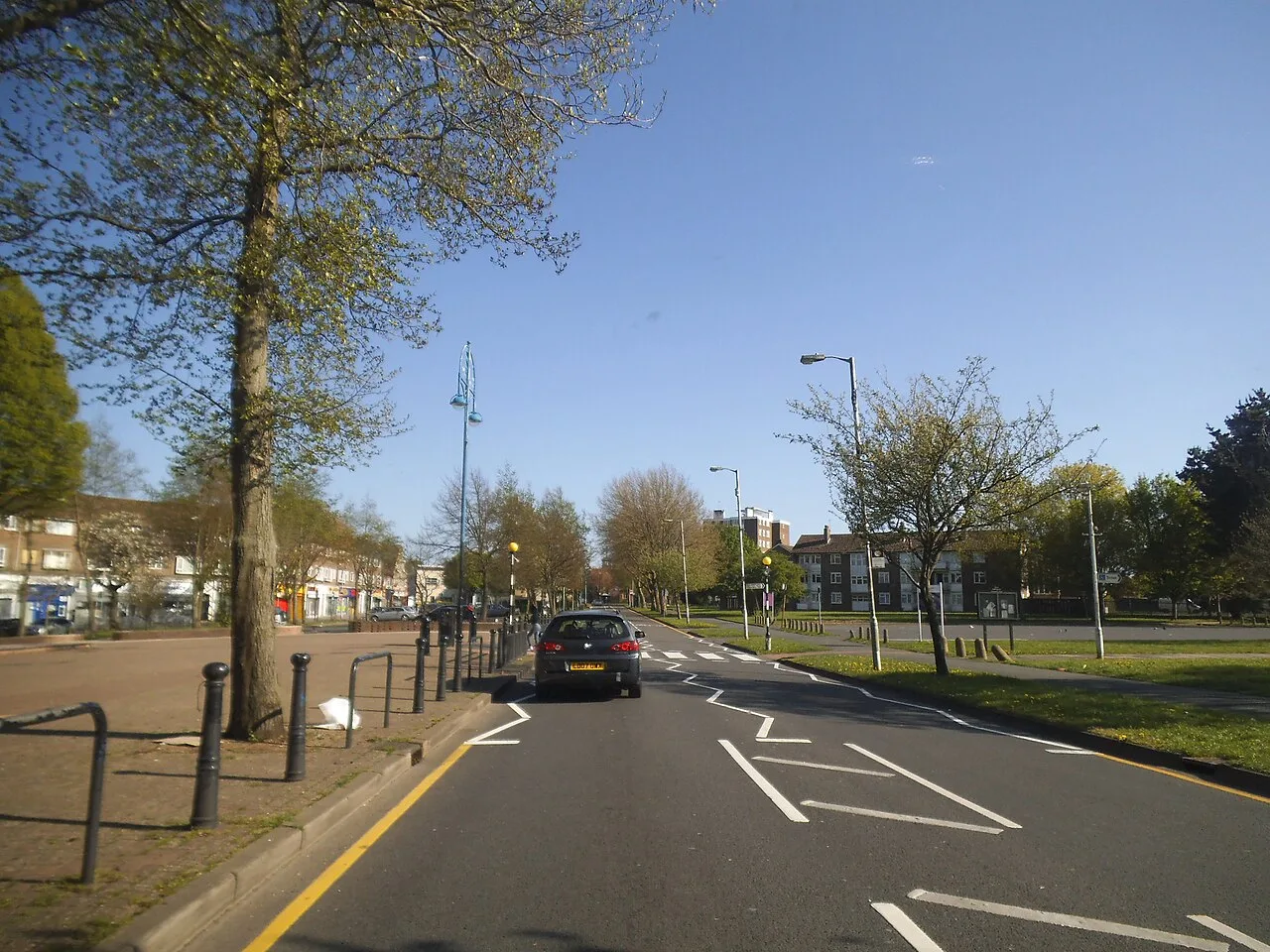 Central Parade in New Addington, a wide tree-lined road with shops on the left and an open paved square