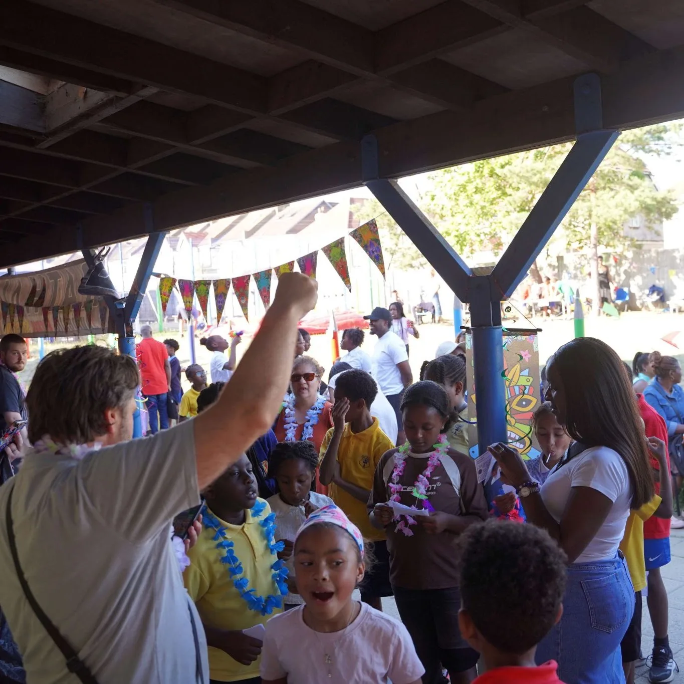 Children, parents and staff gathered under a covered area hung with bunting at the St Cyprian's Summer Fair