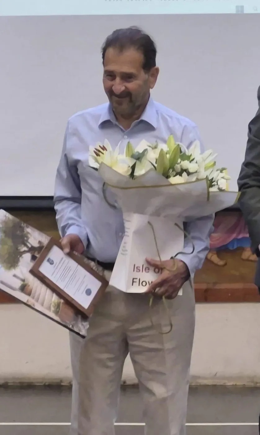 Professor Kypros Nicolaides holding a bouquet of white lilies and a framed certificate at St Cyprian's